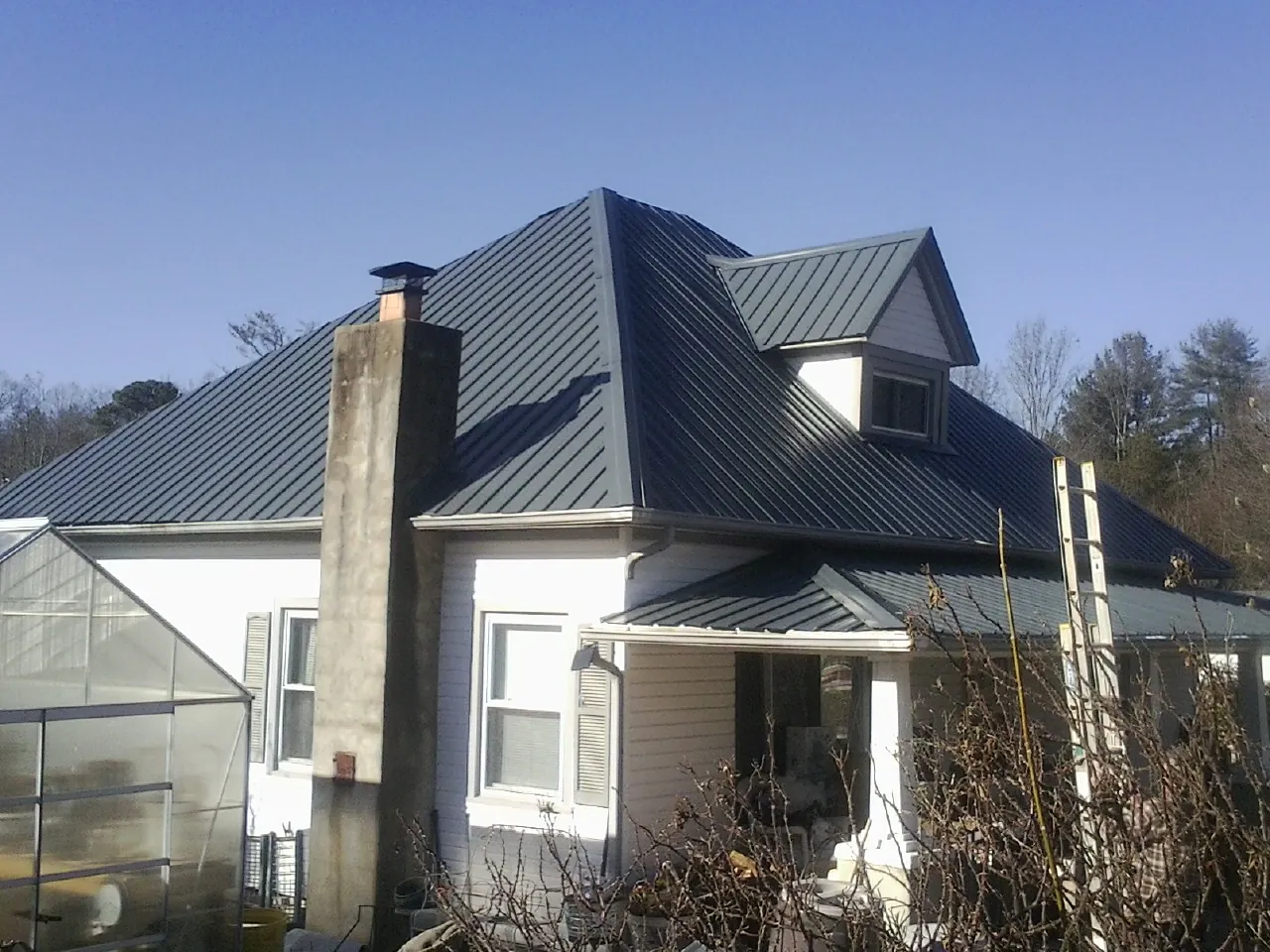 Dark blue standing seam metal roof on a white farmhouse with dormer — Slate & Tile Roof Repair by Roofing Brothers in Mount Saint Joseph