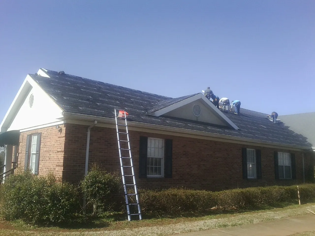 Crew tearing shingles off a brick ranch roof with a ladder set — Emergency Roof Repair work by our crew in Mount Saint Joseph