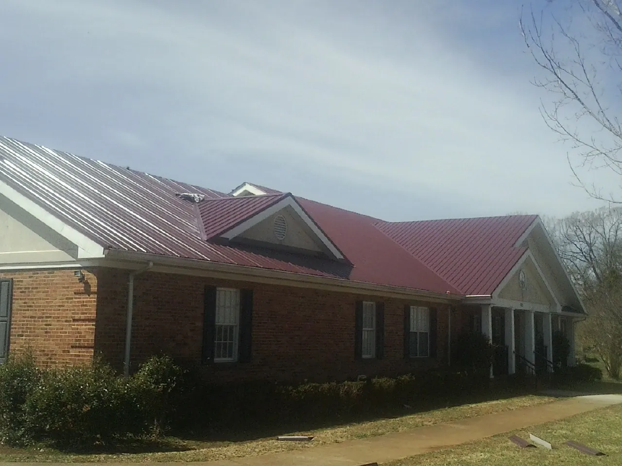 Red metal roof with gabled entries on a long brick building, from a Hail Damage Roof Repair job in Mount Saint Joseph