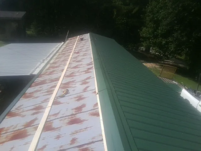Old rusted panels beside newly installed green metal roofing — Wind Damage Roof Repair by Roofing Brothers in Mount Saint Joseph