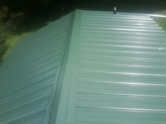 New green metal panels meeting at the ridge of a roof — Flat Roof Repair work by our crew in Mount Saint Joseph