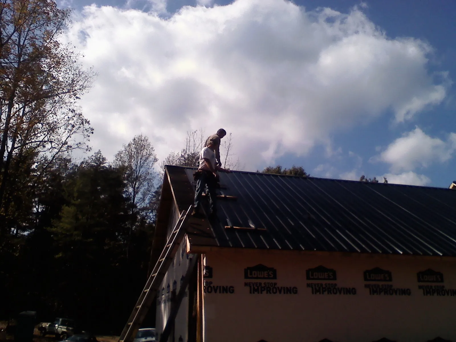 Roofer fastening dark metal panels high against a cloudy sky, from a Roof Inspection job in Mount Saint Joseph