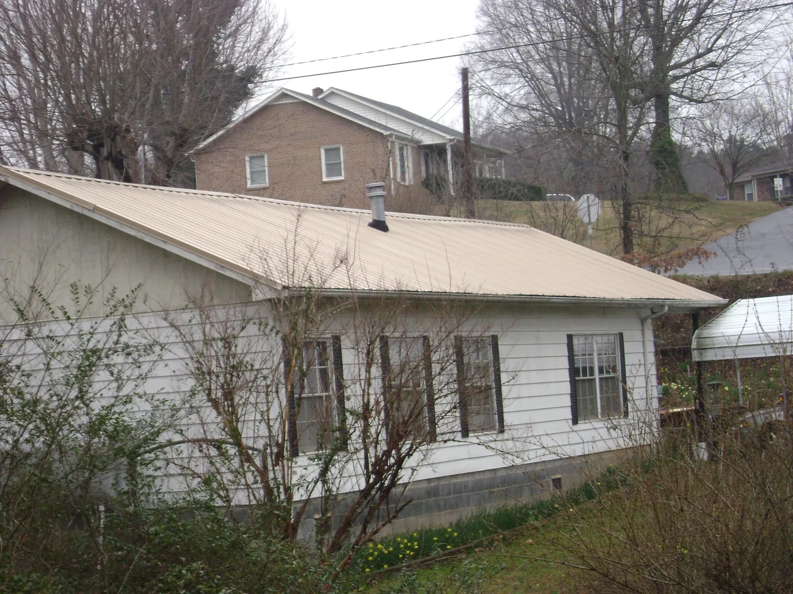 Tan metal roof on a white sided house set into a hillside — Commercial Roofing by Roofing Brothers in Mount Saint Joseph
